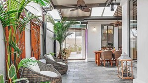 A covered patio area with wicker furniture, potted plants, and a dining table with chairs. - The Port Terrace (Echuca)