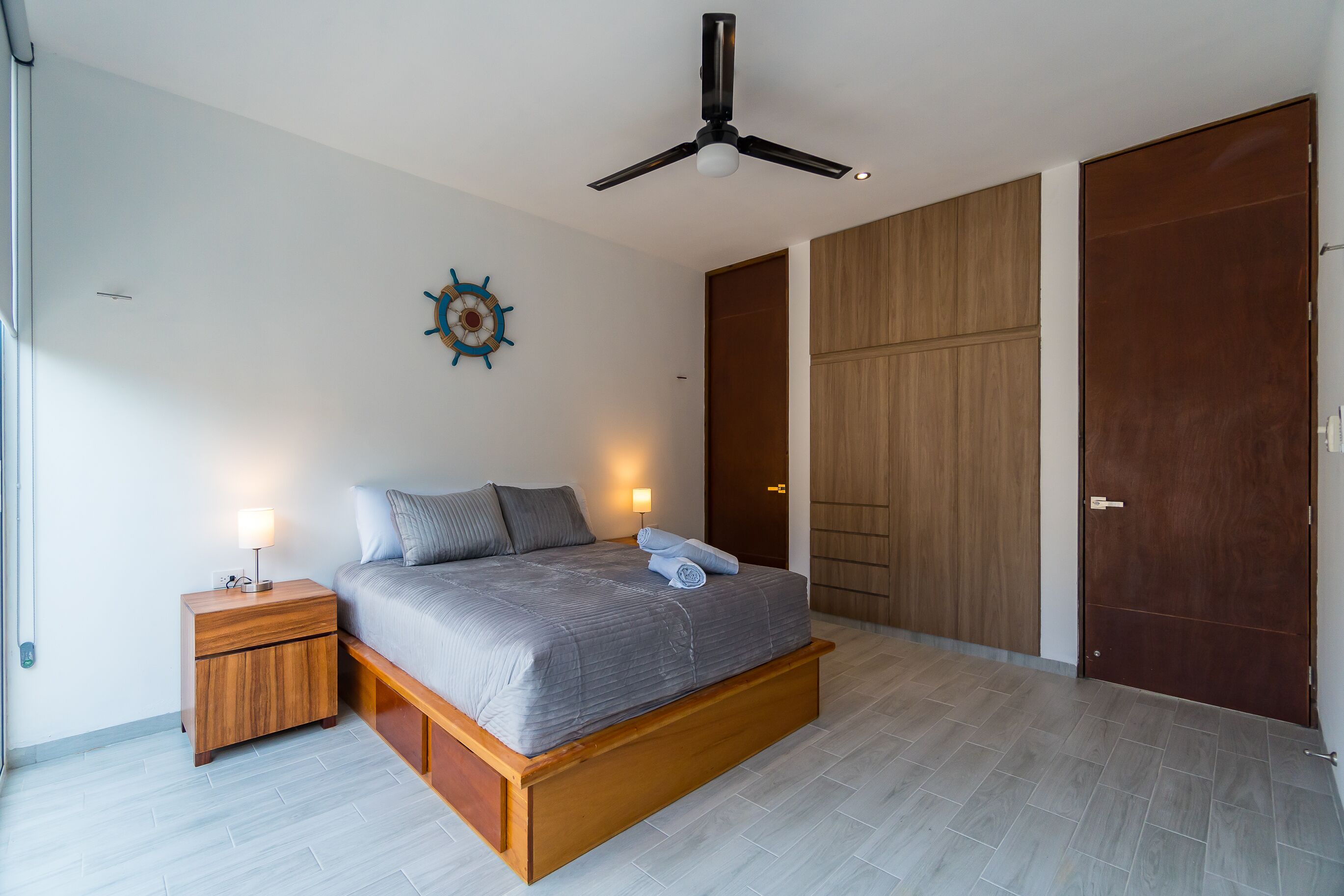 Um quarto moderno com cama, mesas de cabeceira, ventoinha no teto e armário de madeira.