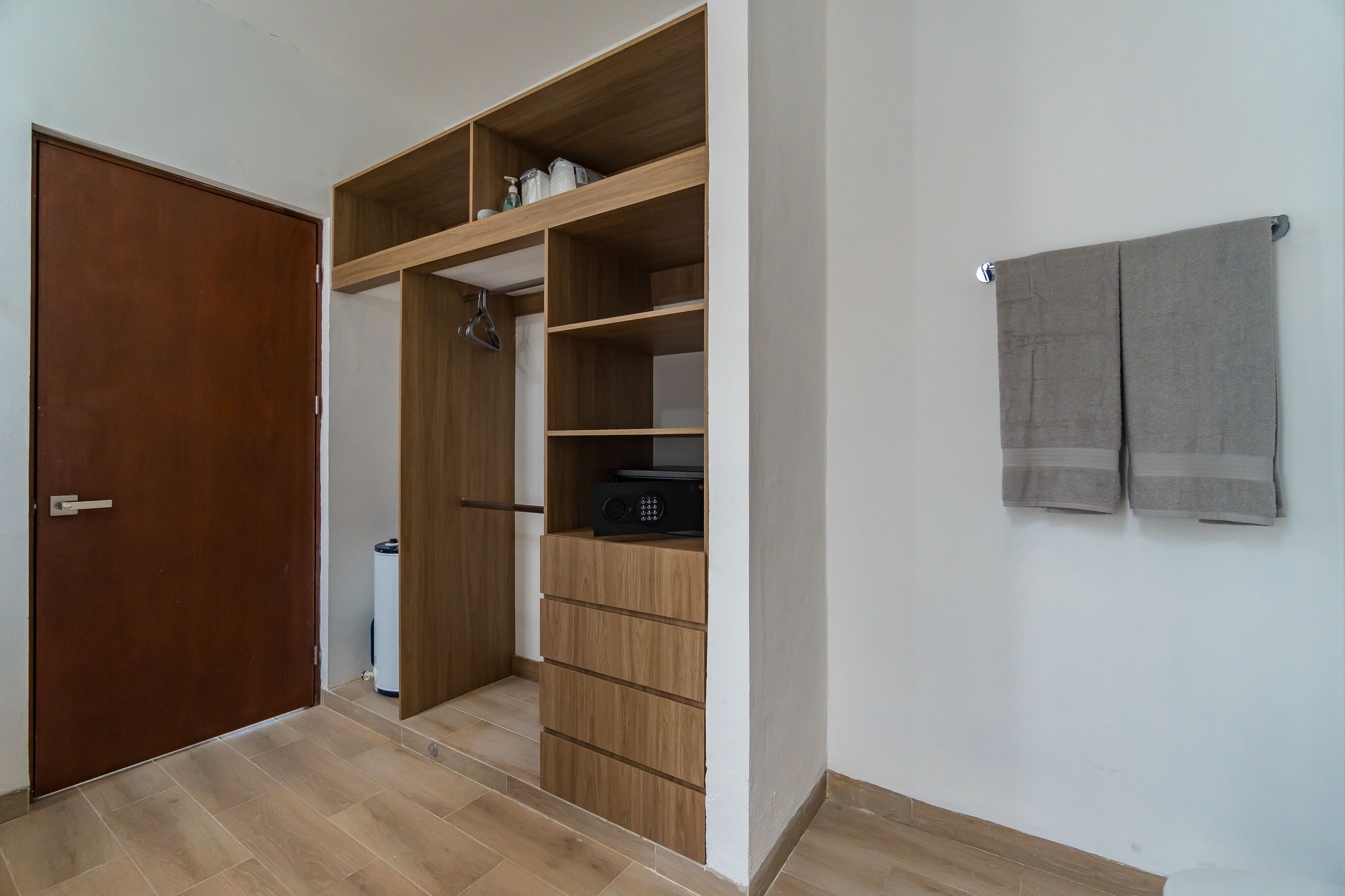 Une pièce avec une armoire en bois, une petite poubelle et une serviette accrochée au mur.