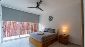 Un dormitorio moderno con una cama grande, un ventilador de techo, una mesita de noche con lámpara y un adorno en la pared.