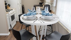 Een eetgedeelte met een ronde tafel voor vier personen, witte kasten, een fornuis en een koelkast op de achtergrond.