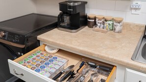 Een keuken met een Keurig koffiezetapparaat, potten met koffiebonen, een lade met bestek en een aanrecht.