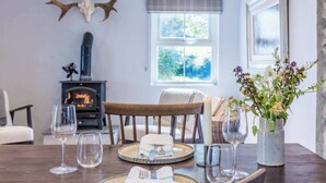 A dining area with a wooden table set for four, a fireplace, and a window with a view of greenery. - Stone Barn (Skibbereen)