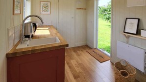 A kitchen with a wooden countertop, a sink, and a door leading to a garden. - Stone Barn (Skibbereen)