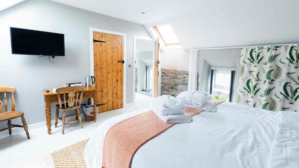 A bedroom with a bed, a TV, a desk, and a window with curtains. - Stone Barn (Skibbereen)