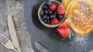A plate with pancakes, blueberries, and strawberries, accompanied by a fork and knife on a wooden surface.