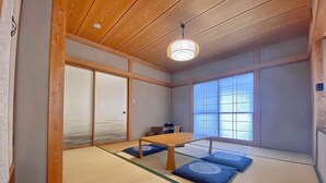 A traditional Japanese room with tatami flooring, a low wooden table, sliding doors, and a large window.