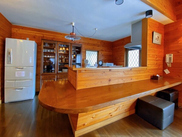 A modern kitchen with wooden cabinetry, a built-in refrigerator, and a bar area with stools.