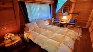 A cozy log cabin bedroom with a large bed, a small table with a lamp, and a chair.
