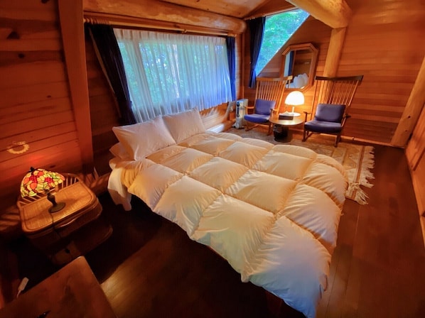 Un dormitorio rústico de madera con una cama grande, una mesita con lámpara y una silla.
