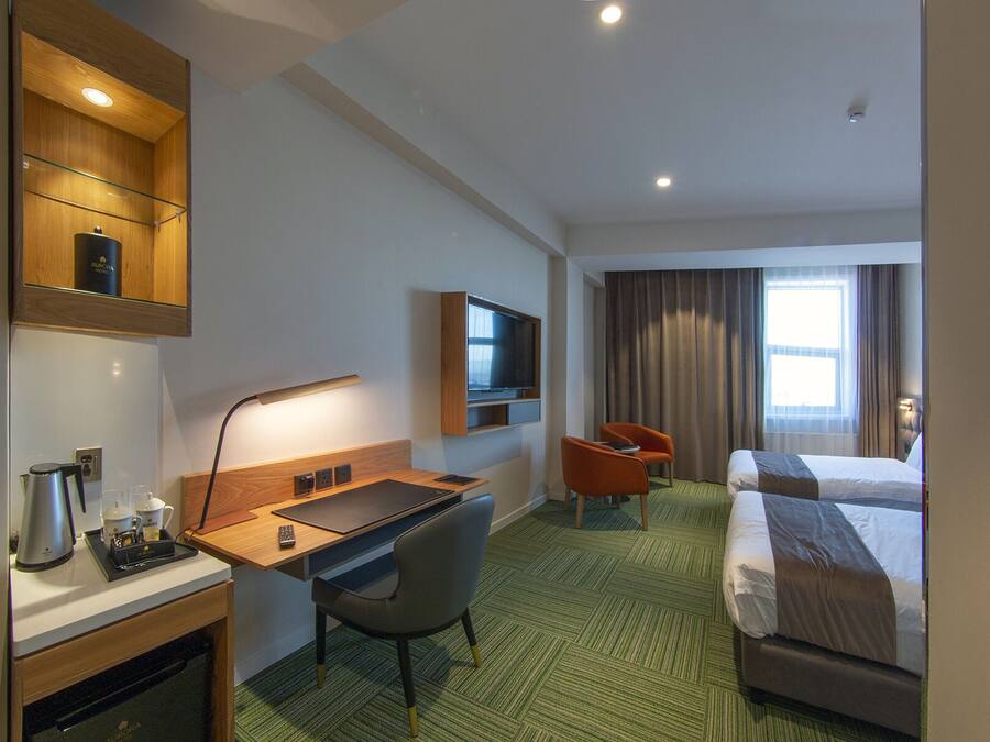 A hotel room with a bed, a desk with a chair, a television, and a minibar.
