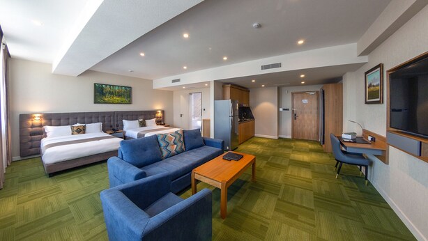 Una habitación de hotel con cama, sofá, escritorio, televisión y zona de cocina.