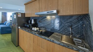 Cocina compacta con armarios de madera, microondas integrado, cafetera y lavamanos con salpicadero de mármol.