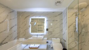 Un baño moderno con piso de mármol, ducha con cerramiento de vidrio, lavamanos blanco y un inodoro.