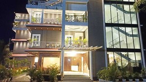 Un hotel de varios pisos con un diseño moderno, que cuenta con balcones, una escalera y una entrada bien iluminada.