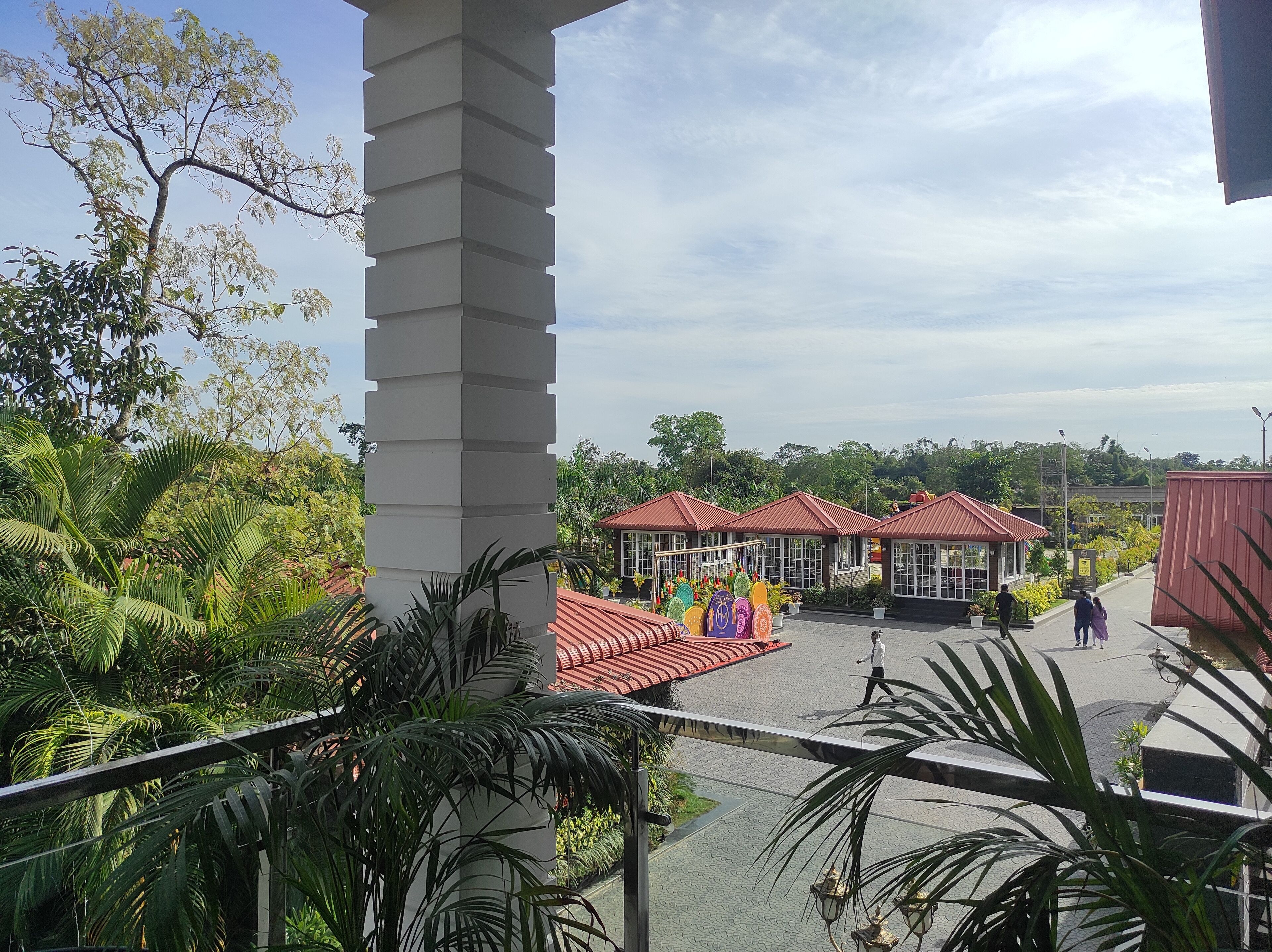 A view of a building with multiple red-roofed structures, surrounded by lush greenery and a clear sky.