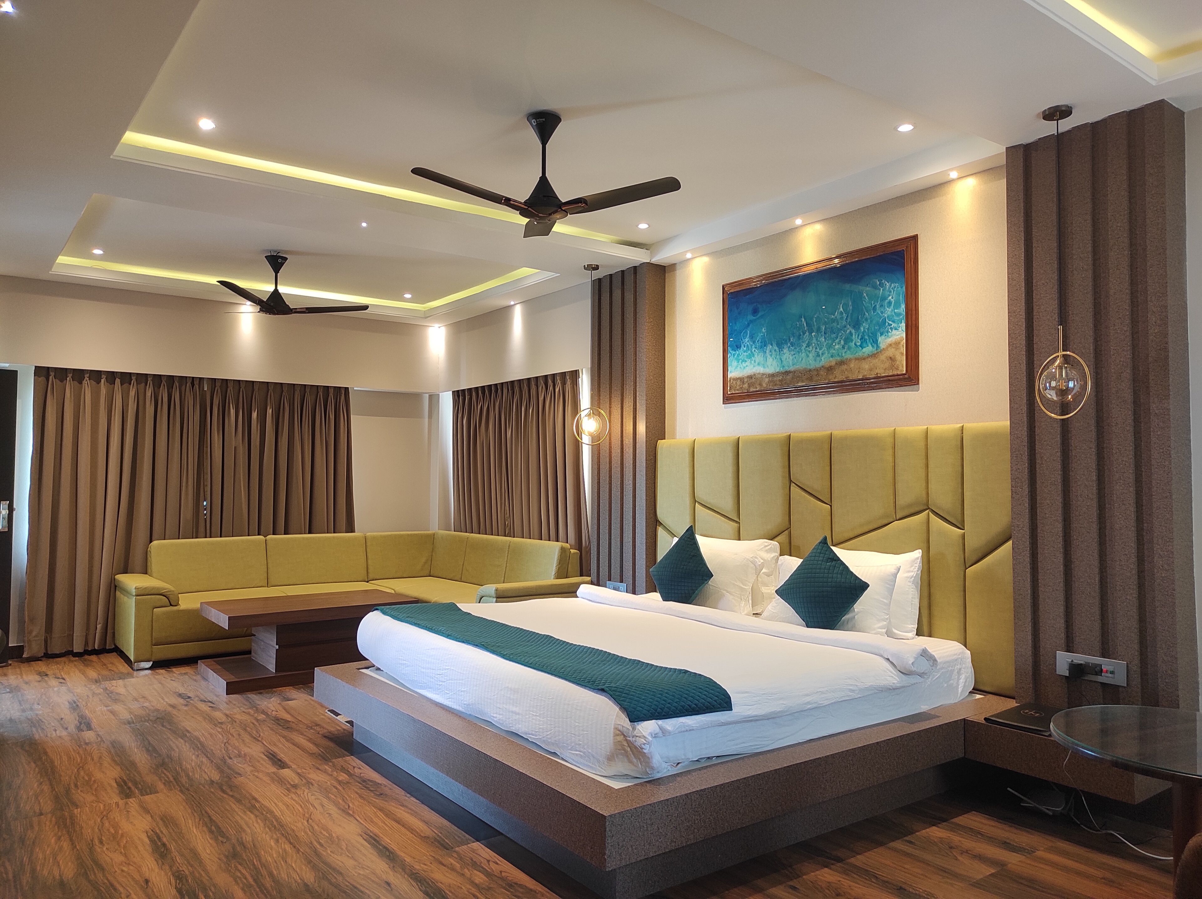 A modern hotel room with a large bed, a sofa, a ceiling fan, and a painting on the wall.