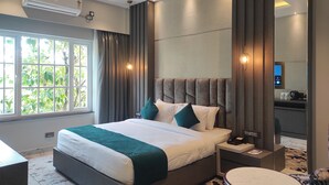Una habitación de hotel moderna con una cama grande, una mesita de noche, una mesa redonda y vistas al verde exterior.