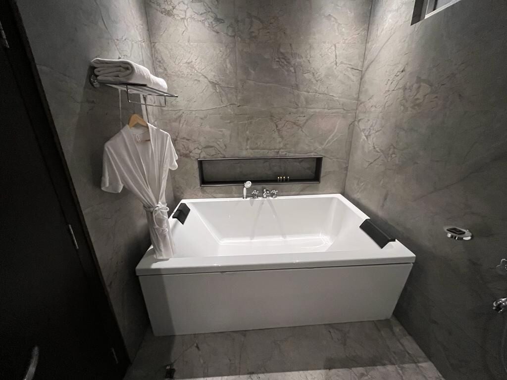 A modern bathroom with a large bathtub, a towel rack with folded towels, and a shelf with toiletries.