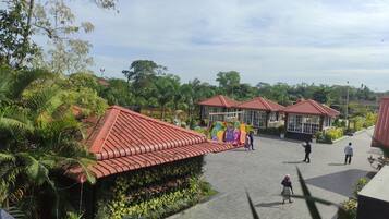A courtyard with red-roofed buildings, surrounded by lush greenery and palm trees.