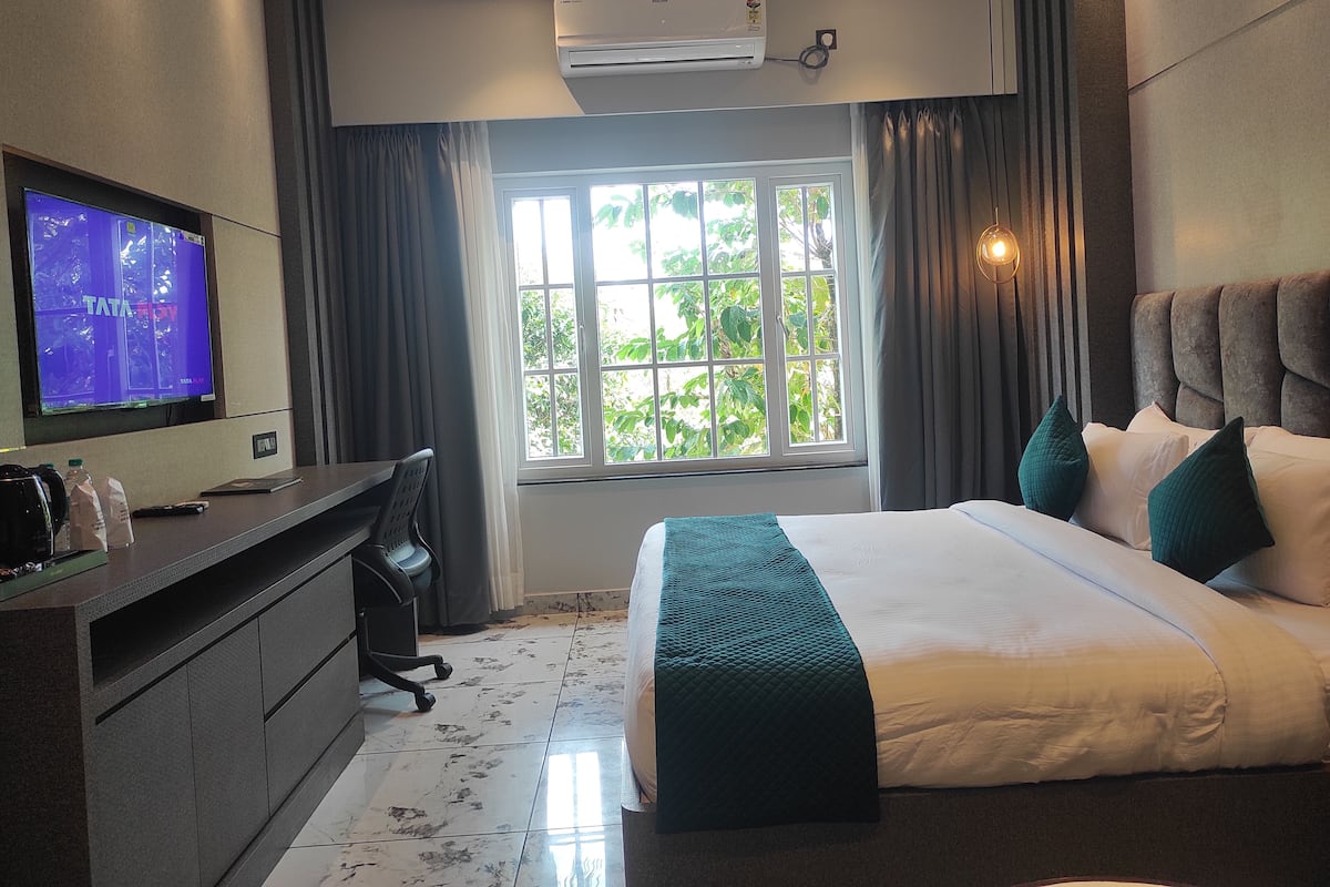 Habitación de hotel con cama, escritorio con computadora, televisor y ventana con cortinas.