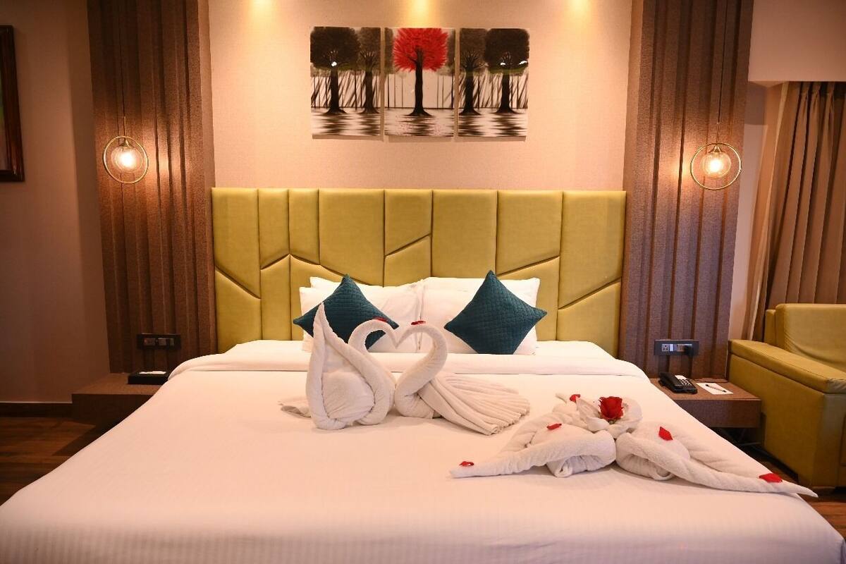 Habitación de hotel con una cama grande, un cabecero tapizado en verde y un cuadro de árboles en la pared.