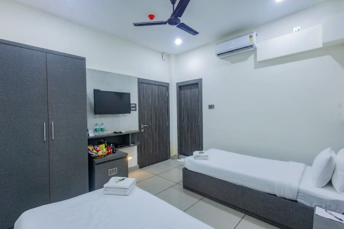 Una habitación de hotel moderna con dos camas, televisor, armario y ventilador de techo.