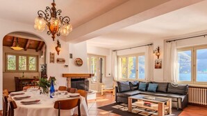 A spacious living area with a fireplace, a dining table set for four, and a sofa facing a large window overlooking a scenic view.