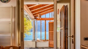 A room with a stone-tiled floor, a wooden table, and a view of a body of water through large windows.