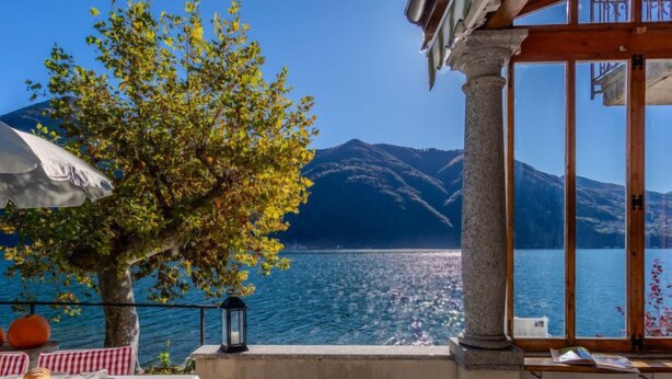A terrace with a table set for dining, a tree, and a view of a lake with mountains in the background.