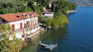 A lakeside property with a dock, a white building with a red roof, and surrounding greenery.