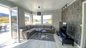 Ett modernt vardagsrum med en hörnsoffa, ett runt soffbord, en tv och en accentvägg i sten.