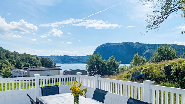 En terrass med ett bord och stolar, med utsikt över en sjö och berg.