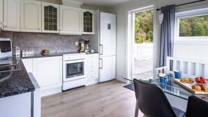 A modern kitchen with white cabinets, a granite countertop, and a glass dining table with chairs. - Heggland Huset by Interhome (Tysnes)