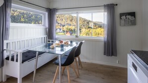 A room with a glass dining table, two chairs, a white bed, and a view of a forested area through large windows. - Heggland Huset by Interhome (Tysnes)