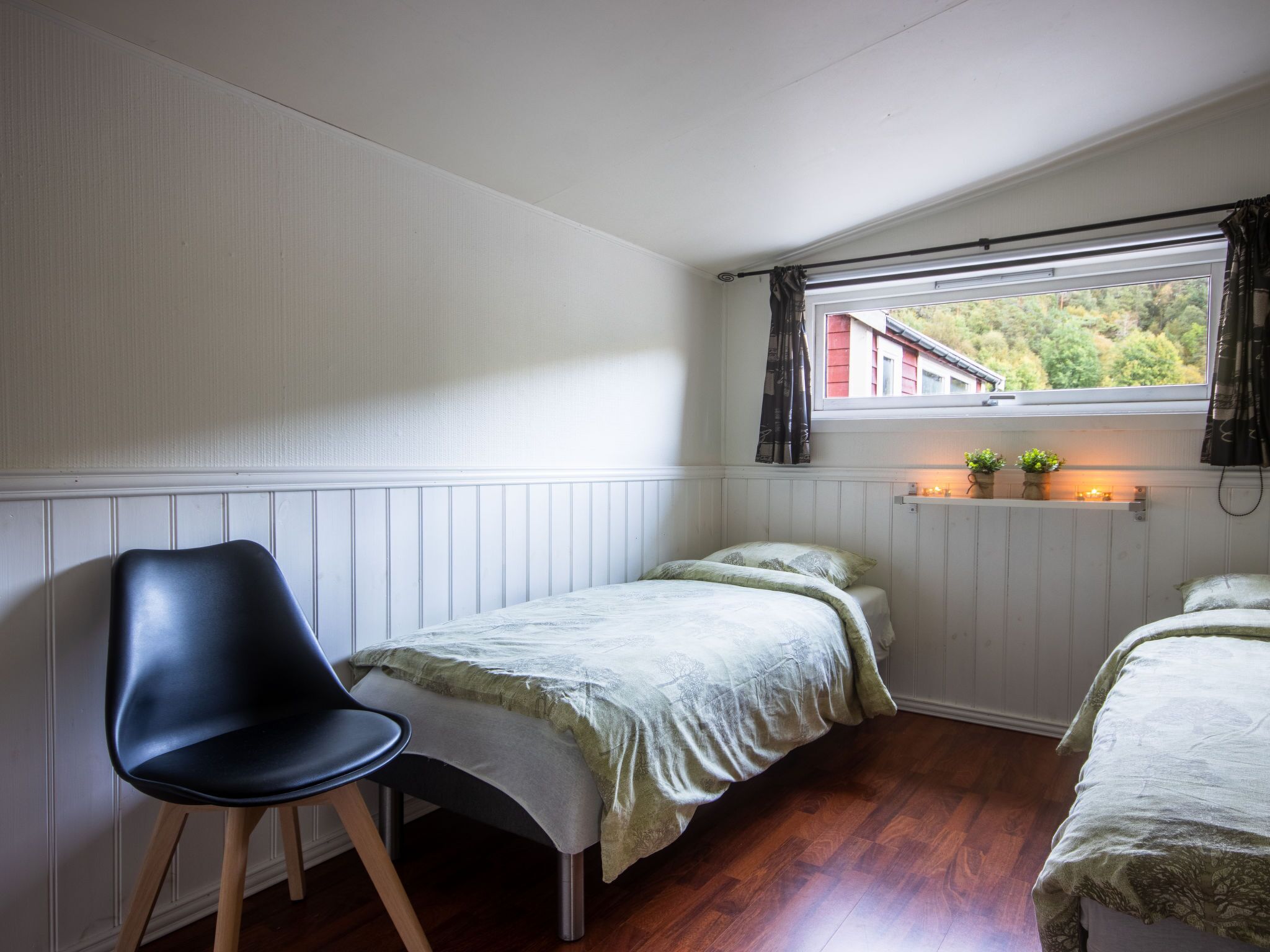 Una camera da letto con due letti singoli, una sedia, una finestra con tende e uno scaffale con piante.
