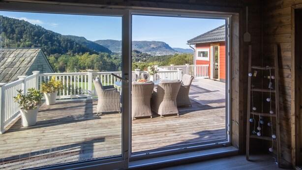 A wooden deck with wicker furniture and potted plants, overlooking a mountainous landscape. - Heggland Huset by Interhome (Tysnes)