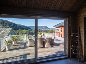 Terraza de madera con muebles de mimbre y plantas en macetas, con vistas a un paisaje montañoso.