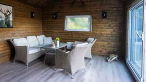 A cozy wooden cabin interior with wicker furniture, a glass table, and a large window offering a view of the outdoors. - Heggland Huset by Interhome (Tysnes)