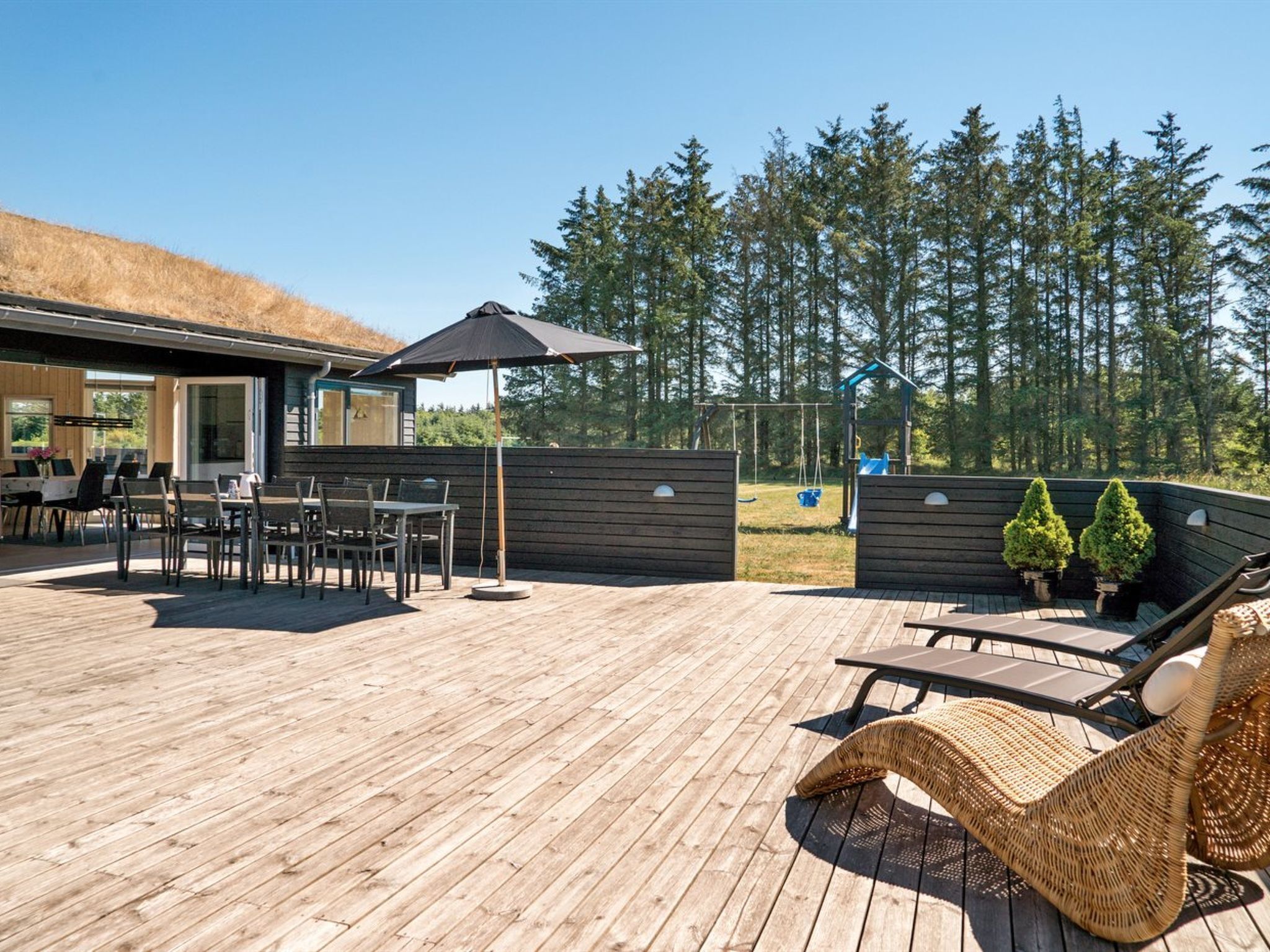 A wooden deck with outdoor furniture, a swing set, and a view of a forest.