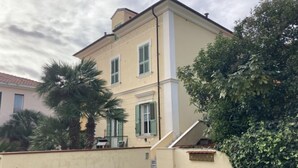 Un bâtiment à deux étages, doté d’une façade beige, de volets verts et d’un escalier apparent menant à l’étage supérieur.