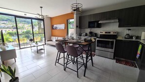Una cocina moderna con armarios oscuros, una isla grande con taburetes de bar, una mesa de comedor y vistas a un paisaje verde a través de amplias ventanas.