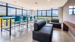 Un salón moderno con un amplio ventanal que ofrece vistas a la ciudad, un espacio de estar con sofás y sillones, y un banco de madera.