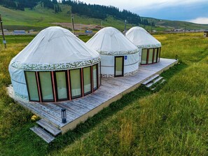 Three yurts with a wooden deck and large windows, set in a grassy field with a hilly background. - Karkyra glamping (Karkara)