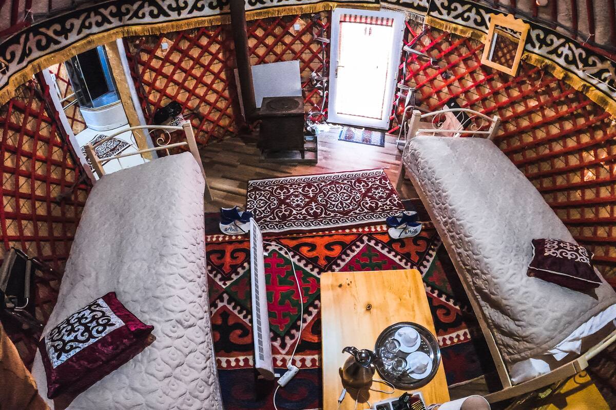 A yurt interior with two white cushioned benches, a patterned rug, a wooden table with a teapot, cups, and a tray.