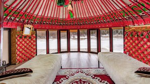 A traditional yurt with two beds, a red patterned ceiling, and a view of a snowy landscape.