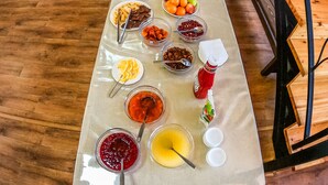 A long table with various food items and condiments, a kitchen area in the background, and a wooden staircase with a metal railing.