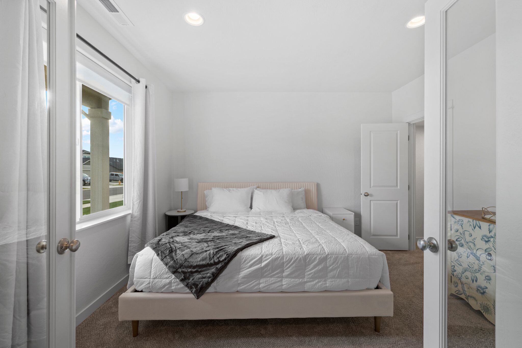 A bedroom with a bed, bedside tables, a nightstand, a window, and a door.