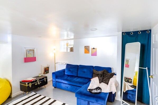 Una habitación con un sofá azul, un baúl dorado y negro, un tapete a rayas y un espejo.