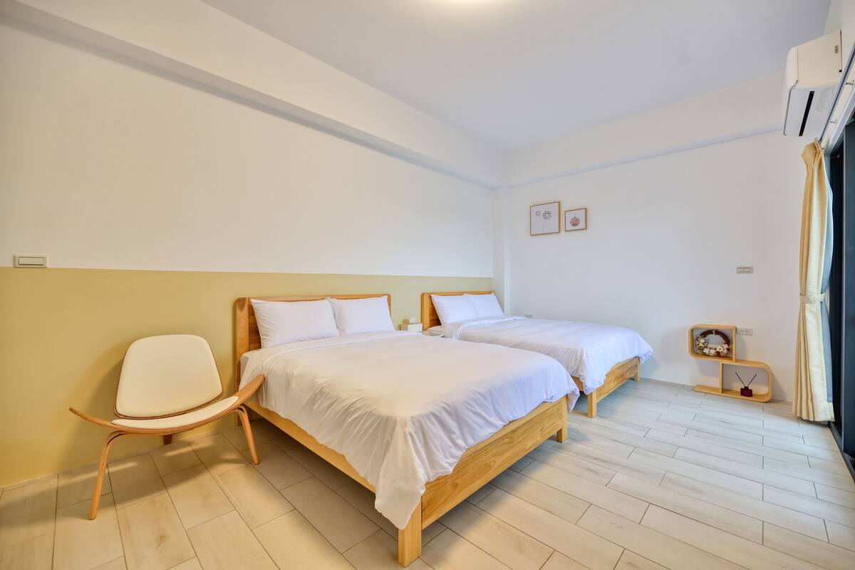 A room with two wooden beds, a white chair, and a small shelf with a decorative item.